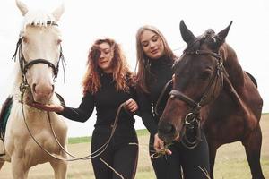 deux belles jeunes filles en train de monter près de leurs chevaux. ils aiment les animaux photo