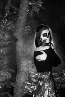 portrait de Jeune femme avec effrayé Halloween maquillage dans forêt. Halloween faire en haut sucre crâne magnifique modèle avec parfait coiffure. diable fille concept. photo