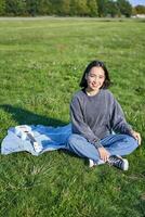 verticale coup de souriant asiatique fille séance sur couverture avec ukulélé guitare, relaxant sur ensoleillé journée en plein air, repos dans parc photo