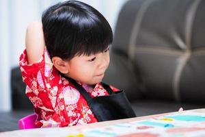 un enfant mignon cherche son dos en se grattant le dos à cause des démangeaisons causées par une étiquette attachée à ses vêtements. petite fille portant une chemise rouge et un tablier noir. photo