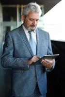 homme d'affaires senior avec tablette à l'extérieur d'un immeuble de bureaux moderne. photo