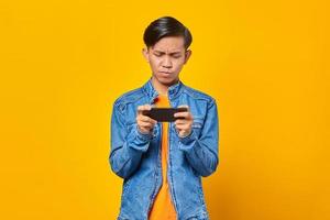 homme asiatique utilisant un téléphone portable jouant au jeu avec un visage en colère sur fond jaune photo
