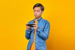 homme asiatique utilisant un téléphone portable jouant au jeu avec un visage en colère sur fond jaune photo