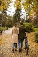 vue arrière au jeune couple dans le parc d'automne avec vélo électrique