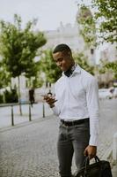 Jeune homme d'affaires afro-américain à l'aide d'un téléphone mobile en attendant un taxi dans une rue photo