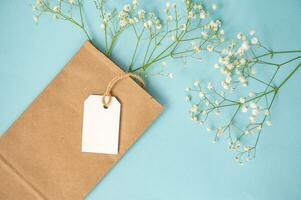 une maquette de une blanc étiqueter, étiquette et prix étiquette près une artisanat sac avec fleurs mensonge sur une coloré Jaune table photo