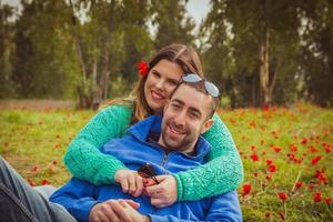 Jeune couple assis sur l'herbe dans un champ de coquelicots rouges et souriant à la caméra photo