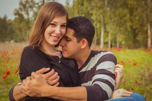 Jeune couple assis sur l'herbe dans un champ de coquelicots rouges et souriant à la caméra photo