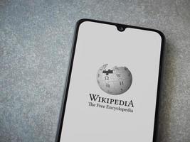 Écran de lancement de l'application wikipedia avec logo sur l'affichage d'un smartphone mobile noir sur fond de pierre céramique