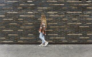 Jeune femme des promenades vers le bas le rue contre une brique mur photo