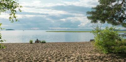 sablonneux plage sur le rive de une vaste lac, une femelle touristique est séance sur une banc fabriqué de vieux palettes photo