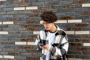 Jeune homme avec une téléphone sur le Urbain Contexte de brique mur photo