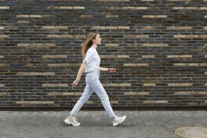 Jeune femme des promenades vers le bas le rue dans de face de une brique mur photo