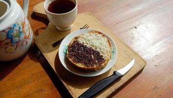 une mini photo d'un martabak avec une garniture au chocolat et du fromage râpé trouvé une tasse est chaude, un couteau, une fourchette et des couverts