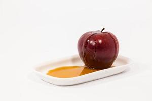 pomme rouge avec des gouttes de miel sur une plaque blanche avec du miel isolé sur fond blanc photo