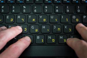 homme tapant sur un clavier avec des lettres en hébreu et en anglais photo