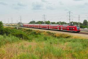 train de voyageurs israélien rouge en mouvement hors de la ville près de l'autoroute 4 photo