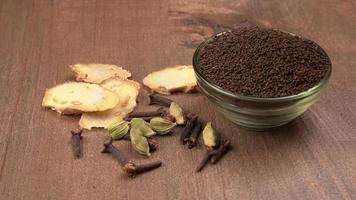 poudre de thé noir ou poudre de thé en poudre sèche, chai patti isolé dans un bol en verre avec cardamome, clou de girofle et gingembre. photo