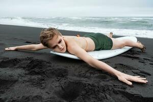 femelle surfeur est mensonge sur planche de surf sur plage avec bras tendu à côtés après surfant formation photo