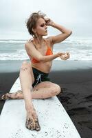 sexy femelle surfeur séance sur planche de surf sur sablonneux plage avec mer vagues dans Contexte photo
