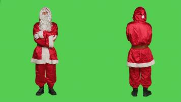 Saint pseudo en riant sur caméra, posant dans rouge costume plus de plein corps écran vert. Père Noël cosplay diffusion Noël veille vacances esprit, dépeindre célèbre hiver personnage avec chapeau et lunettes. photo