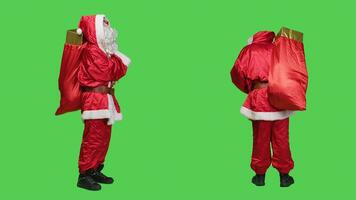 couler pseudo dans costume à la recherche autour, porter gros rouge sac plein de cadeau des boites plus de plein corps écran vert toile de fond. Jeune la personne habillé comme Père Noël diffusion Noël vacances esprit, présente pour enfants. photo