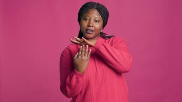 expressif Jeune noir femme montrant temps libre signe en utilisant sa mains dans de face de rose Contexte. africain américain beauté affichage pause signal avec corps Langue vers caméra. photo