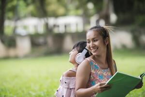 mère et fille lisant un conte de fées à sa fille écoutent le son avec un casque dans le parc photo