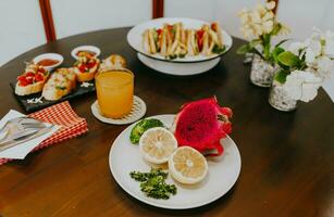 apéritif table avec italien antipasti collations et Orange jus dans lunettes. Frais citron et dragon fruit sur blanc plaque. brushetta ou authentique traditionnel Espagnol tapas ensemble plus de en bois tableau. photo