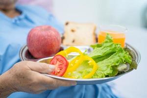 Une patiente asiatique âgée ou âgée de vieille dame mangeant un petit-déjeuner de légumes sains avec espoir et heureuse assise et affamée sur son lit à l'hôpital. photo