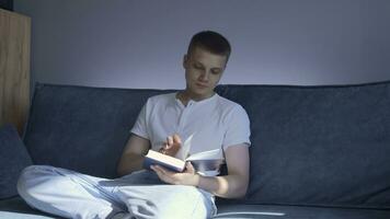 Jeune homme est sérieusement en train de lire livre à maison. médias. Beau homme est en train de lire livre séance sur canapé à maison. Jeune homme est en train de lire livre et engagé dans développement personnel photo