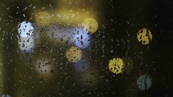 fermer de le flou lumière taches par le fenêtre et gouttes de pluie chute vers le bas sur le verre à le soir. concept. pluvieux temps photo