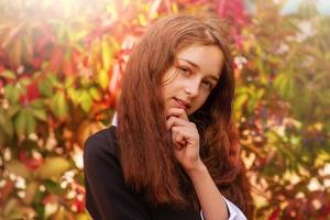 portrait d'une fillette de 11 ans aux cheveux longs à l'automne sur fond de feuilles rouges. écolière photo