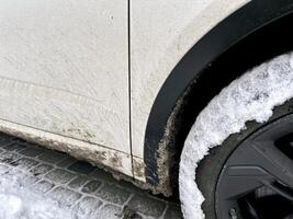 côté vue de blanc voiture avec sale neige tache. voiture sale roue, et porte de le voiture avec marais éclaboussures sur une côté panneau. photo