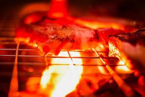grillage porc sur inoxydable acier gril avec flammes sur noir arrière-plan, nourriture et cuisine concept. brûlant porc sur une charbon gril. photo