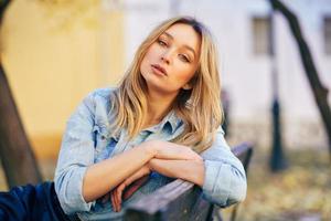 femme blonde portant une chemise en jean et une jupe en cuir noir assis dans un banc urbain. photo