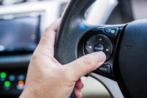 proche en haut main une chauffeur presse le multifonction bouton de voiture sur le pilotage roue utilisation contrôle l'audio et changement joueur la musique photo