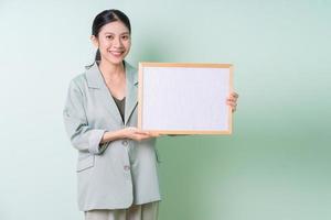 Jeune femme d'affaires asiatique tenant un tableau blanc sur fond vert photo