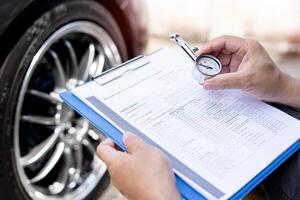 un homme tient un manomètre vérifier la pression d'air des pneus et un mémo dans la liste de contrôle en service contrôle de l'entretien de base de la voiture photo