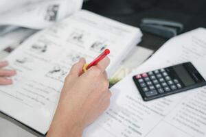 prof utilisation une rouge stylo vérifier exemple feuille et examen équipement sur le bois table et utilisation bureau ordinateur travail dans le Contexte photo