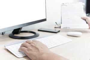 une homme utilisation ordinateur bureau chercher nouvelles sur le l'Internet avec à la recherche une nouvelles papier sur le bois table photo