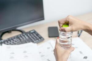 proche en haut main une femmes ouvert l'eau bouteille casquette et examen équipement sur le bois table et utilisation bureau ordinateur travail photo