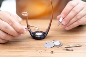 une homme utilisation pinces à serrer le numérique regarder batterie et Tournevis retirer et changement dans réparer cassé montres-bracelets et outil sur bois table photo