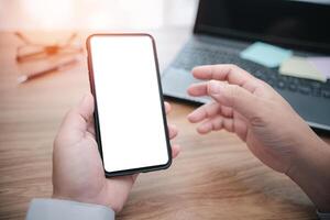 proche en haut blanc afficher de téléphone intelligent dans main affaires homme et portable ordinateur avec bois table dans Contexte photo