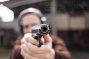 une homme pousse une pistolet, visée à le cible. une homme portant protecteur écouteurs. une mur et une toit avec balle des trous. Extérieur tournage intervalle photo