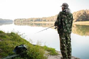 Sénior concept. une pêcheur sur rivière captures prédateur poisson. utile passe-temps, magnifique l'automne, actif en bonne santé mode de vie. arrière vue photo