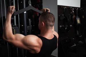 portrait de une Beau Masculin entraîneur dans salle de sport. le athlète Est-ce que un exercice sur le simulateur dans le salle de sport. construit muscle, pièces des sports, une en bonne santé mode de vie. côté vue photo