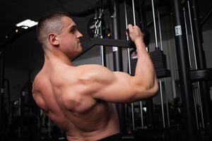 portrait de une Beau Masculin entraîneur dans salle de sport. le athlète Est-ce que un exercice sur le simulateur dans le salle de sport. construit muscle, pièces des sports, une en bonne santé mode de vie. torse photo