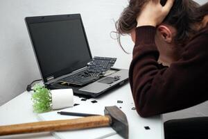 homme détruit portable avec une marteau. nerveux travail, petit chariot ordinateur, les erreurs, lent l'Internet, ne pas enregistré dans le jeu, imprimé texte, suspendu. mal vieux ordinateur échoué, Est-ce que ne pas tour sur, bloque. regrets photo