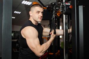 Jeune Beau entraîneur dans une noir uniforme contre Contexte de une simulateur dans salle de sport. musclé athlétique corps de une carrossier, encadrement, individuel des sports et poids perte cours. portrait. pompes mains photo